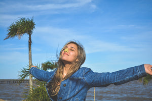 Girl wearing colorful sunscreen on her nose looking up at the sun with her eyes closed and arms open taking in the environment.